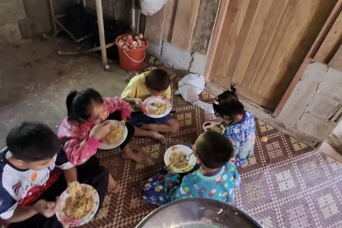 Village children sharing a noodle meal together on a woven mat