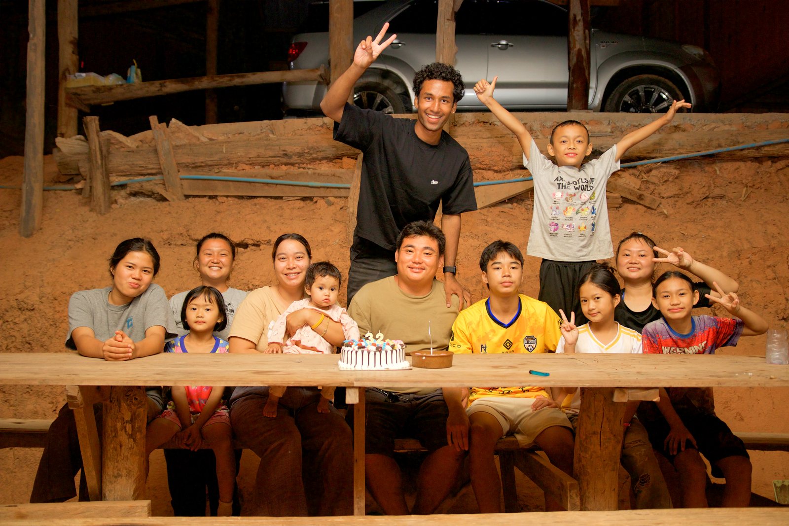 A guest smiling with the village family around a celebration cake