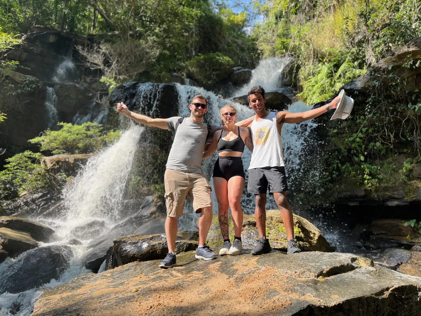 Three guests with arms raised in front of a jungle waterfall